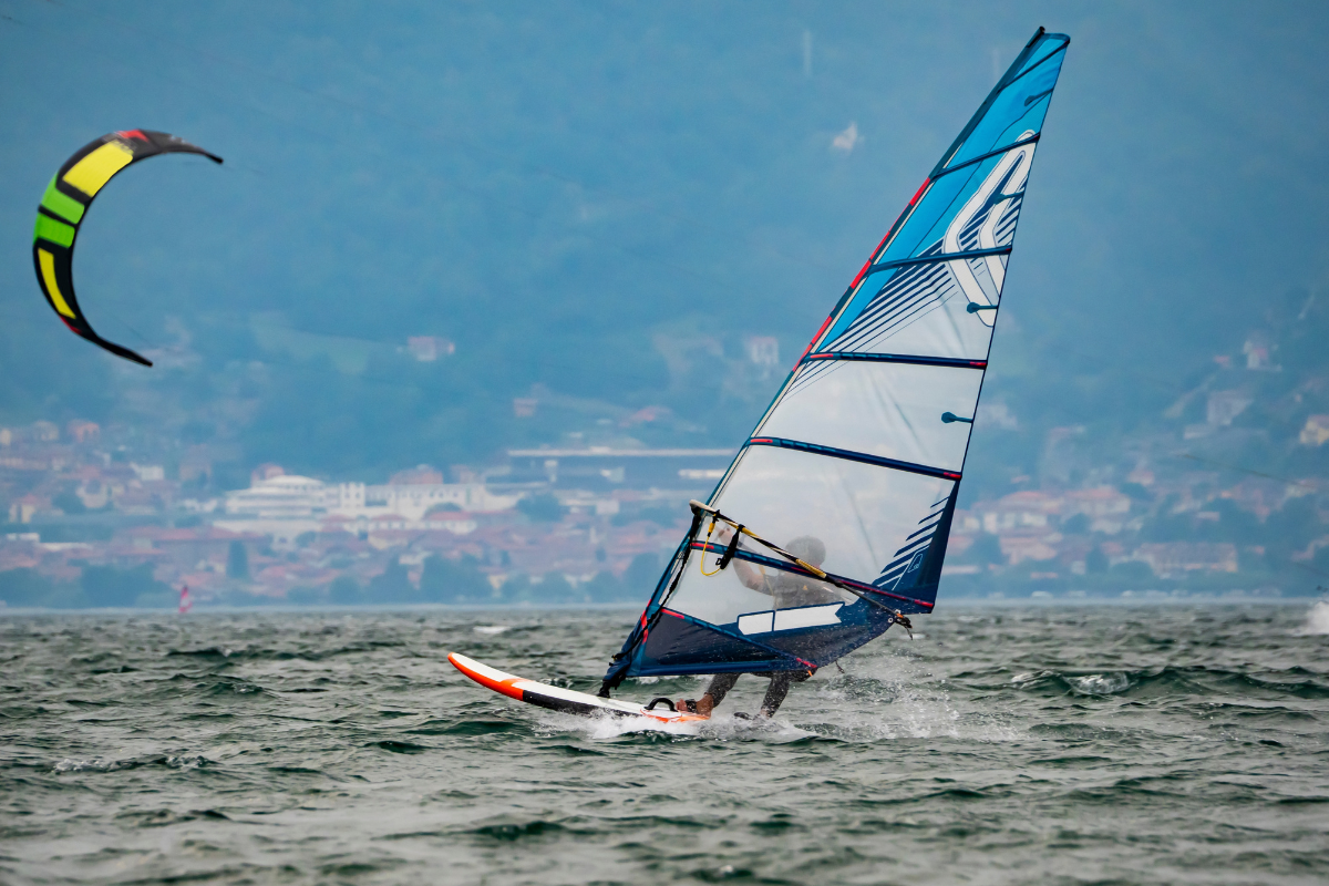 A person wind-surfing on Lake Como, with a kitesurfer behind him.